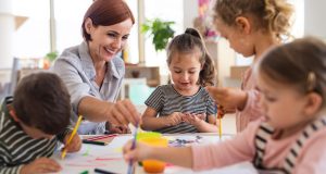 A group of small nursery school children with teacher indoors in classroom, painting.